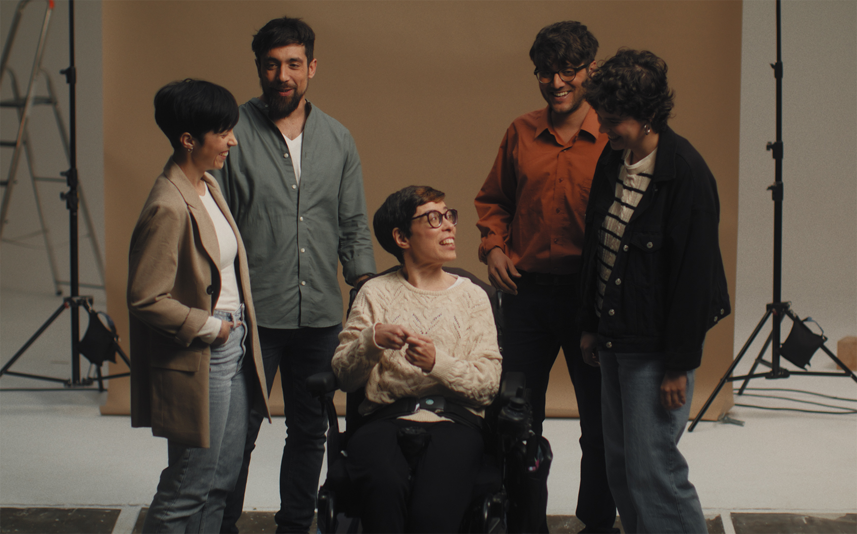 Grupo de cinco personas hablando con una chica en sillas de ruedas en el centro en un estudio de fotografía